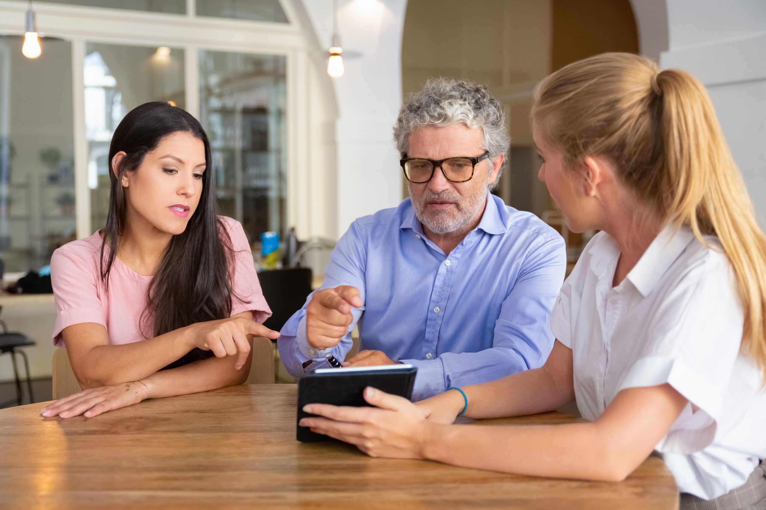 serious-young-woman-mature-man-meeting-with-female-professional-watching-presentation-tablet-po-scaled.jpg
